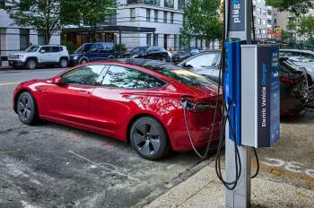A red electric vehicle charging at an EV station on a city street.