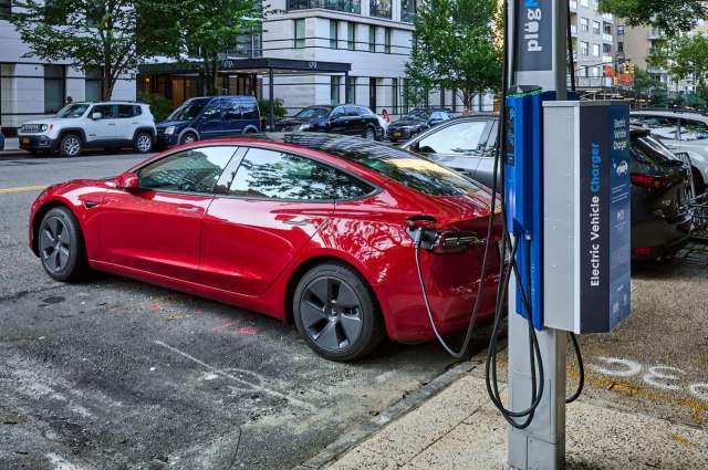 A red electric vehicle charging at an EV station on a city street.