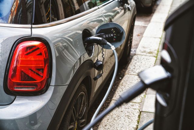 A gray electric vehicle is charging at a station with a cable connected to its charging port.