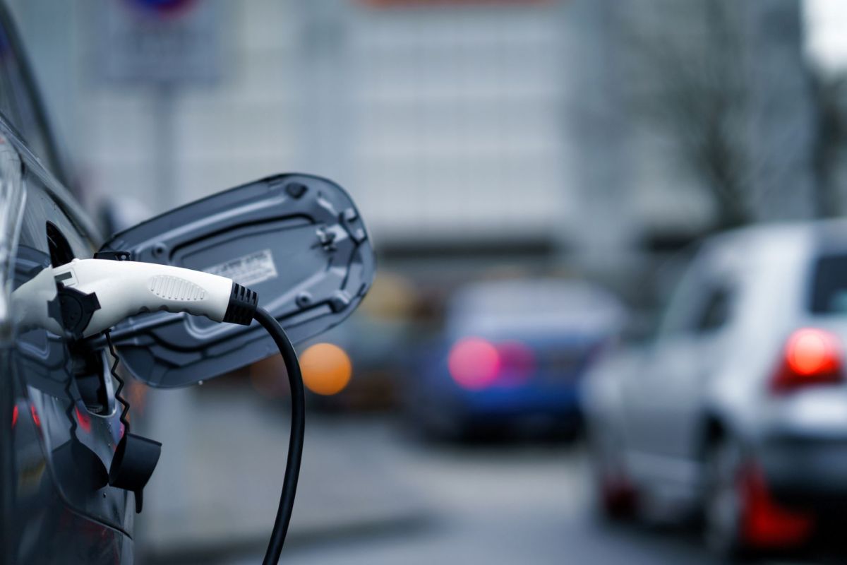 An electric vehicle charging cable is plugged into a car parked on a city street.