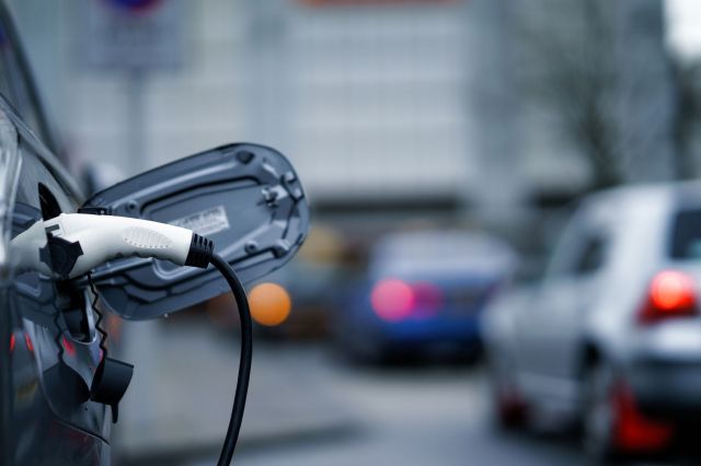 An electric vehicle charging cable is plugged into a car parked on a city street.