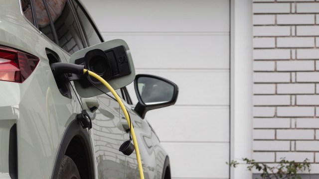 An electric vehicle is charging with a yellow cable connected to its side, parked next to a white brick wall.