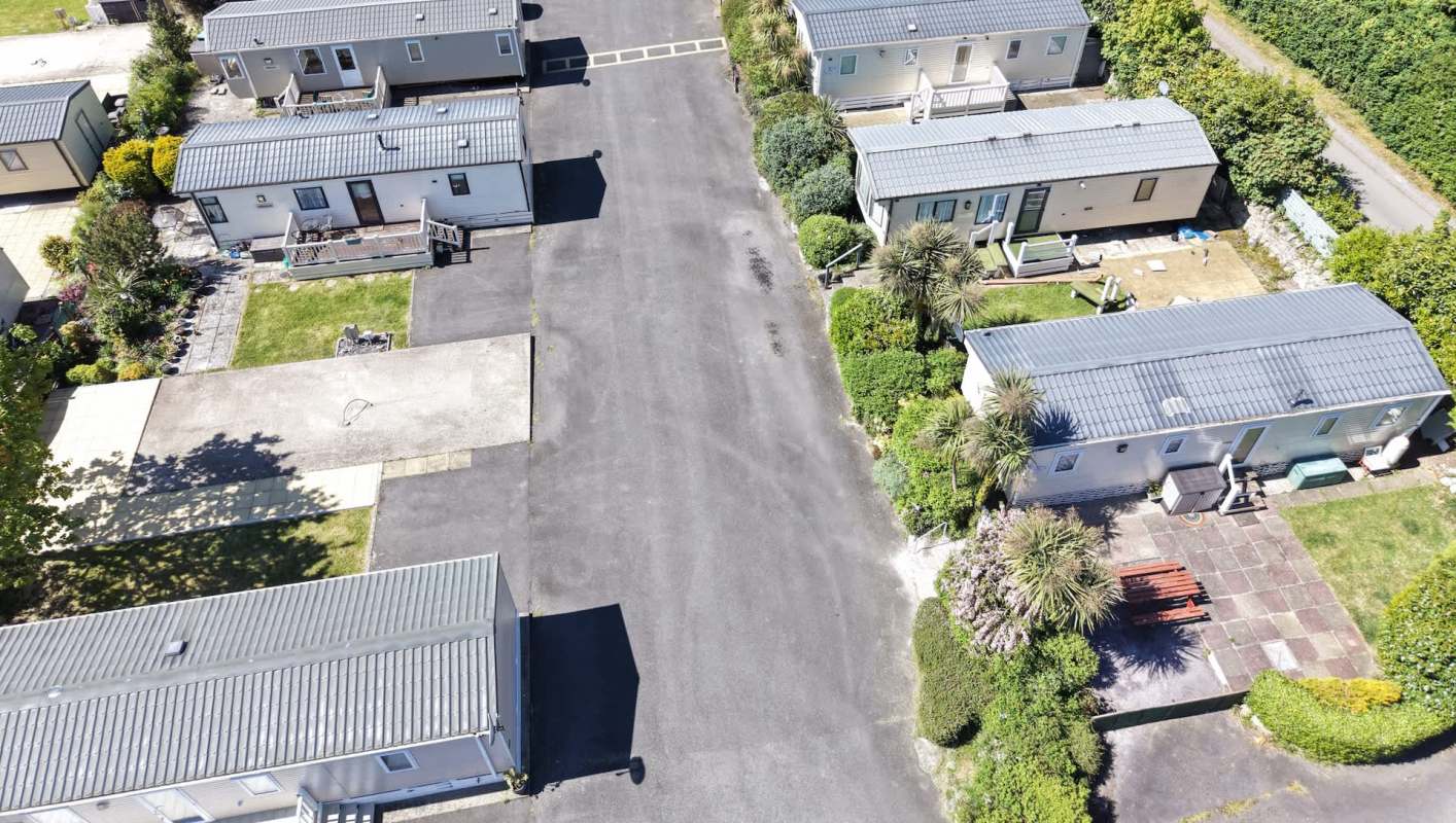 Aerial view of a residential area featuring several mobile homes and surrounding greenery along a paved road.