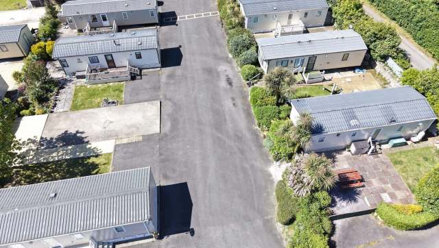 Aerial view of a residential area featuring several mobile homes and surrounding greenery along a paved road.