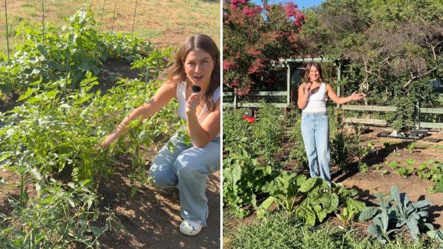 A woman stands in a garden, showcasing vegetables and greenery in bright sunlight.