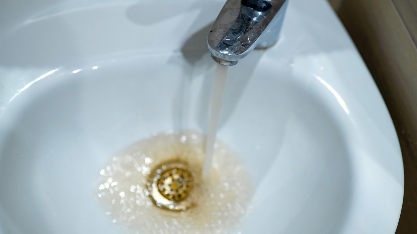 Water is flowing from a faucet into a sink, creating bubbles with a brownish tint.
