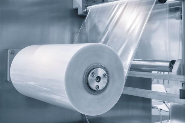 A roll of transparent film being processed in a machine.