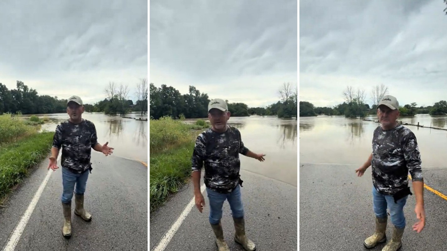 A man in boots stands on a flooded road.