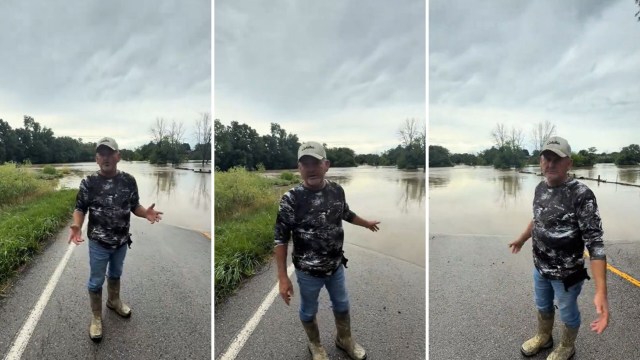 A man in boots stands on a flooded road.