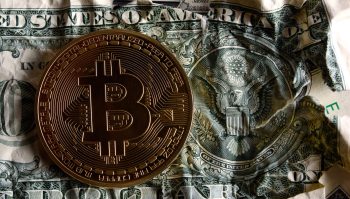 A Bitcoin coin resting on a crumpled one-dollar bill, symbolizing cryptocurrency and traditional currency.