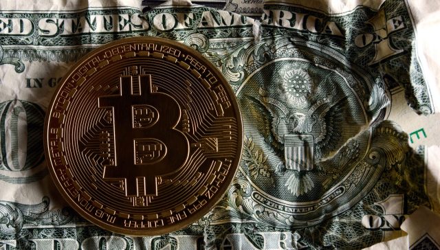 A Bitcoin coin resting on a crumpled one-dollar bill, symbolizing cryptocurrency and traditional currency.
