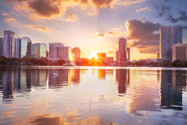 A sunset over a city skyline with reflecting water and swans in the foreground.