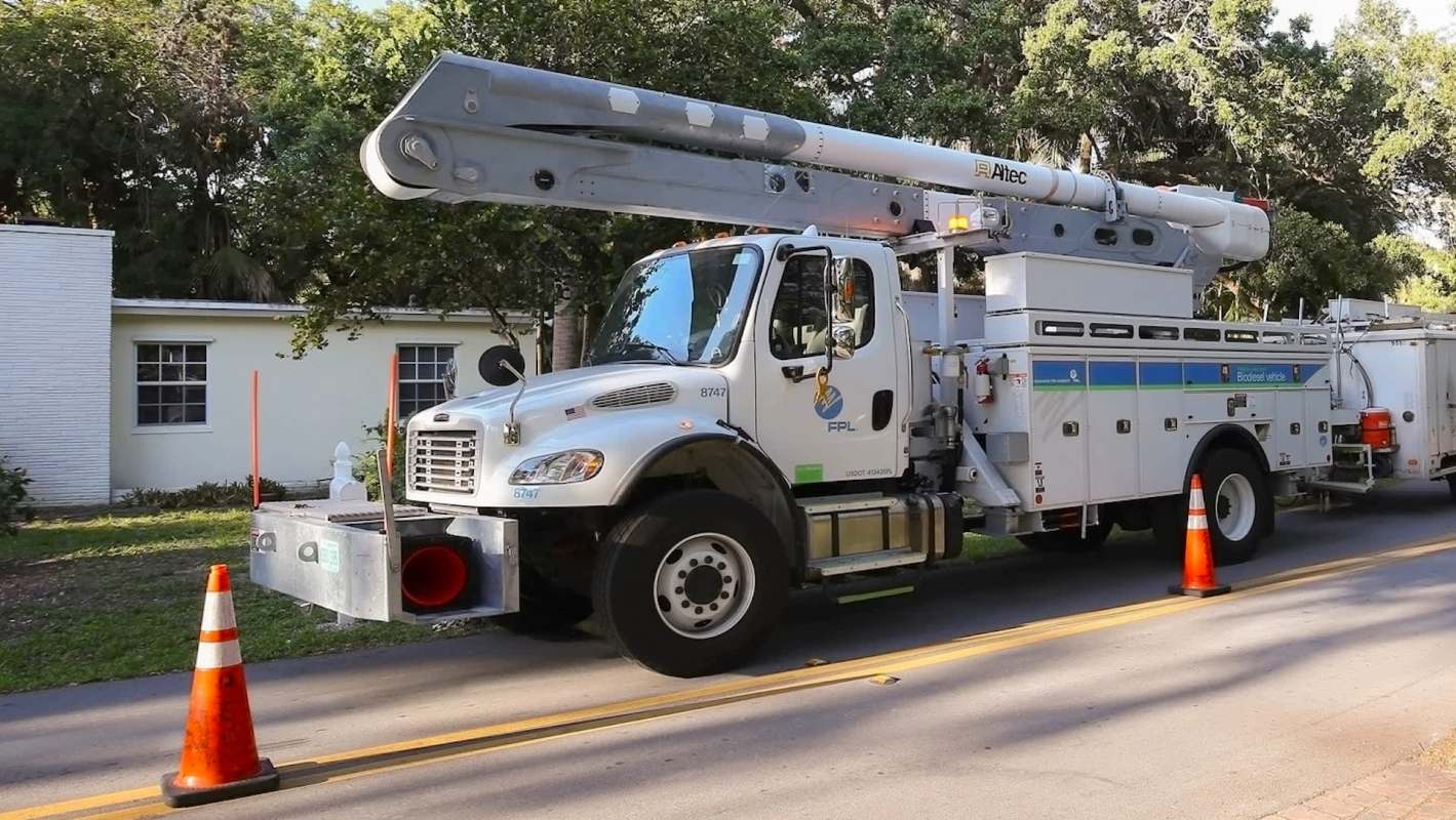 A utility truck with an FPL logo parked on a residential street near traffic cones.