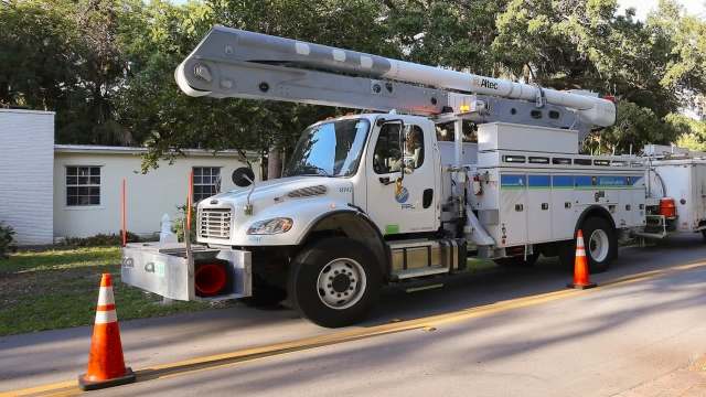 A utility truck with an FPL logo parked on a residential street near traffic cones.