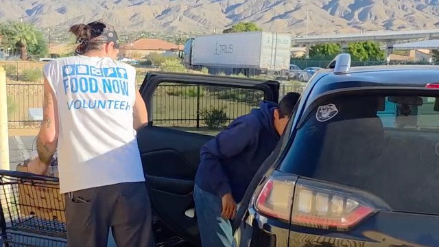 A volunteer helps a person load items into an SUV at a food distribution site.