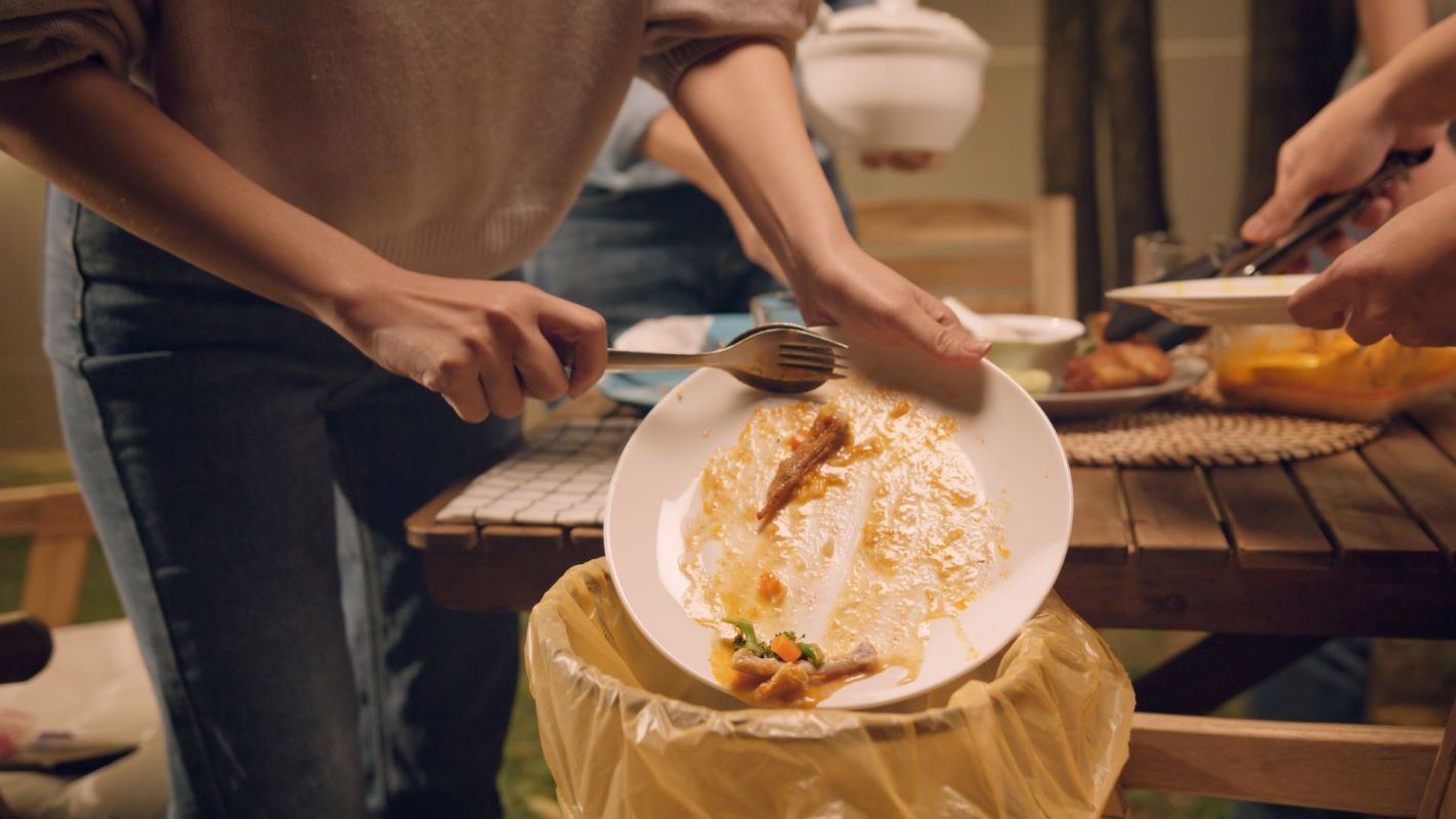 A person scraping food into a trash can.