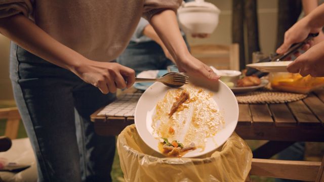 A person scraping food into a trash can.