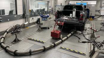 A pickup truck in a testing facility connected to exhaust measurement equipment and monitoring systems.
