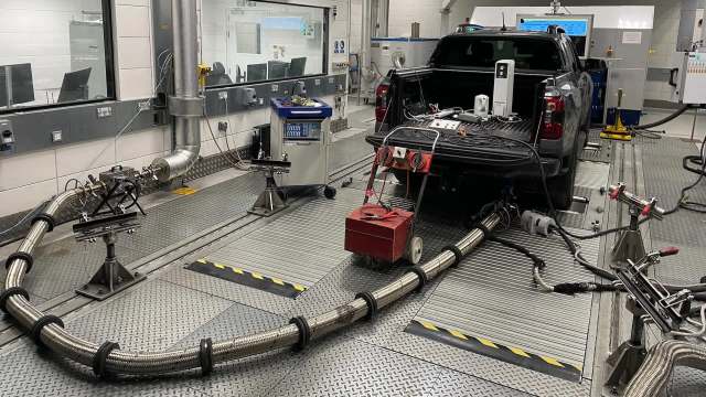 A pickup truck in a testing facility connected to exhaust measurement equipment and monitoring systems.
