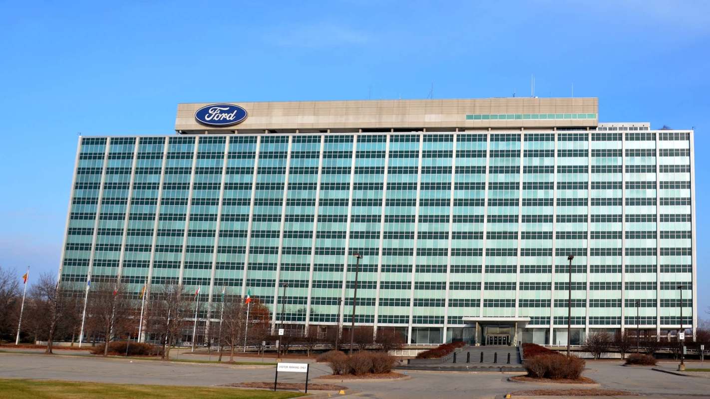 A large, modern office building with green-tinted windows and a Ford logo on top.