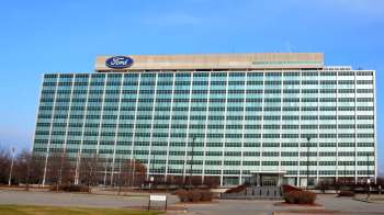 A large, modern office building with green-tinted windows and a Ford logo on top.