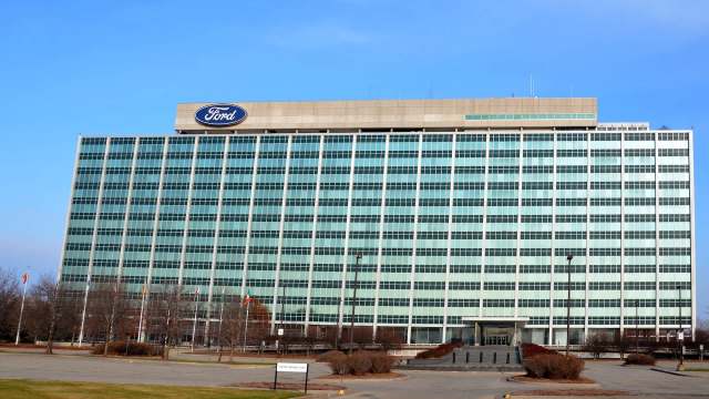 A large, modern office building with green-tinted windows and a Ford logo on top.