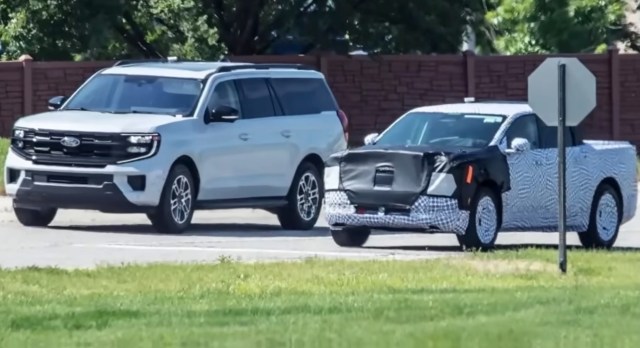 A silver SUV and a camouflaged pickup truck at a stop sign.