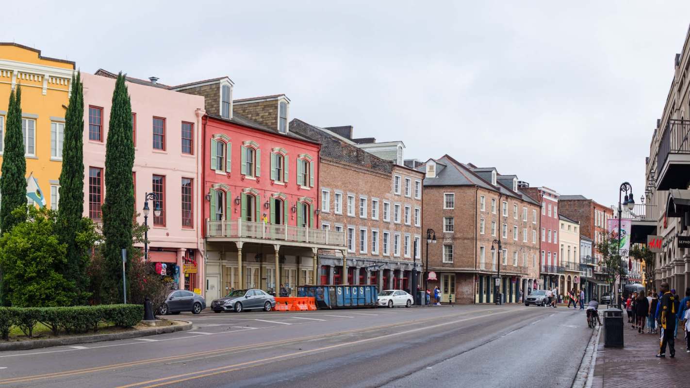 Colorful historic buildings line a street with pedestrians and parked cars on a cloudy day.