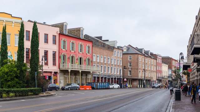 Colorful historic buildings line a street with pedestrians and parked cars on a cloudy day.