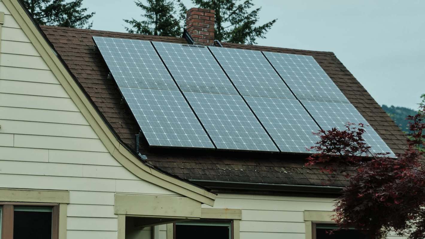A house with solar panels installed on the roof, surrounded by greenery.