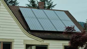 A house with solar panels installed on the roof, surrounded by greenery.