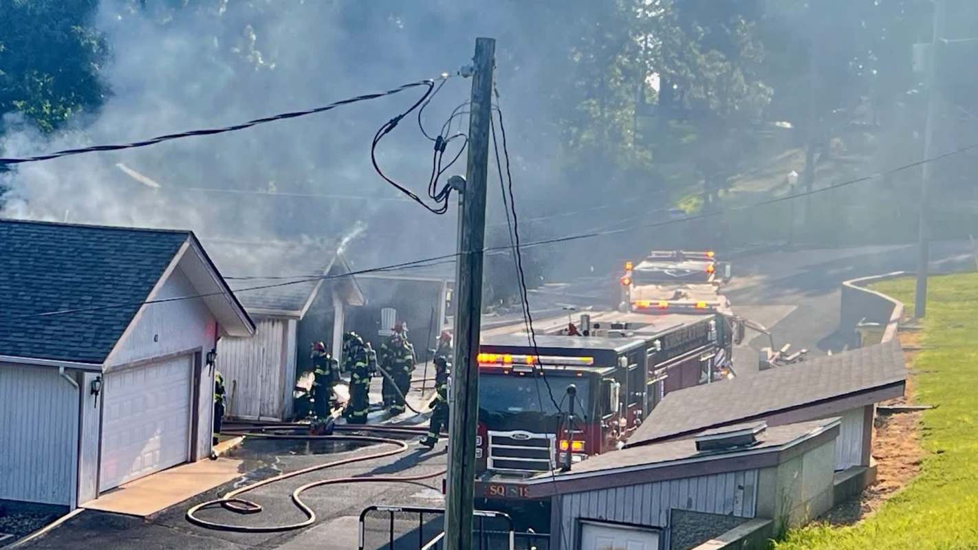 Firefighters respond to a building fire, surrounded by smoke and emergency vehicles on the scene.