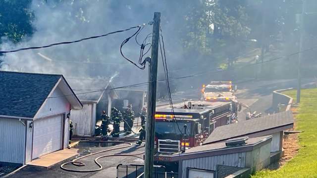 Firefighters respond to a building fire, surrounded by smoke and emergency vehicles on the scene.