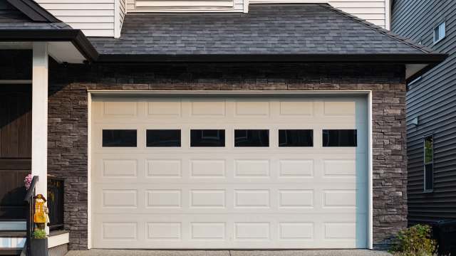 A cream-colored garage door with window panels, set against a stone and wooden house exterior.
