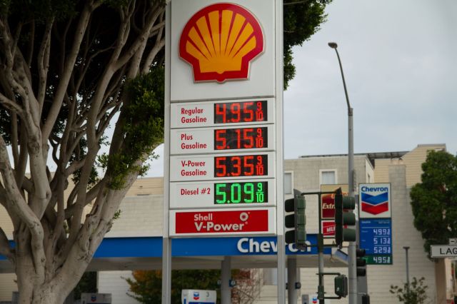 A gas station sign displays fuel prices: Regular $4.95, Plus $5.15, V-Power $5.35, and Diesel #2 $5.09.