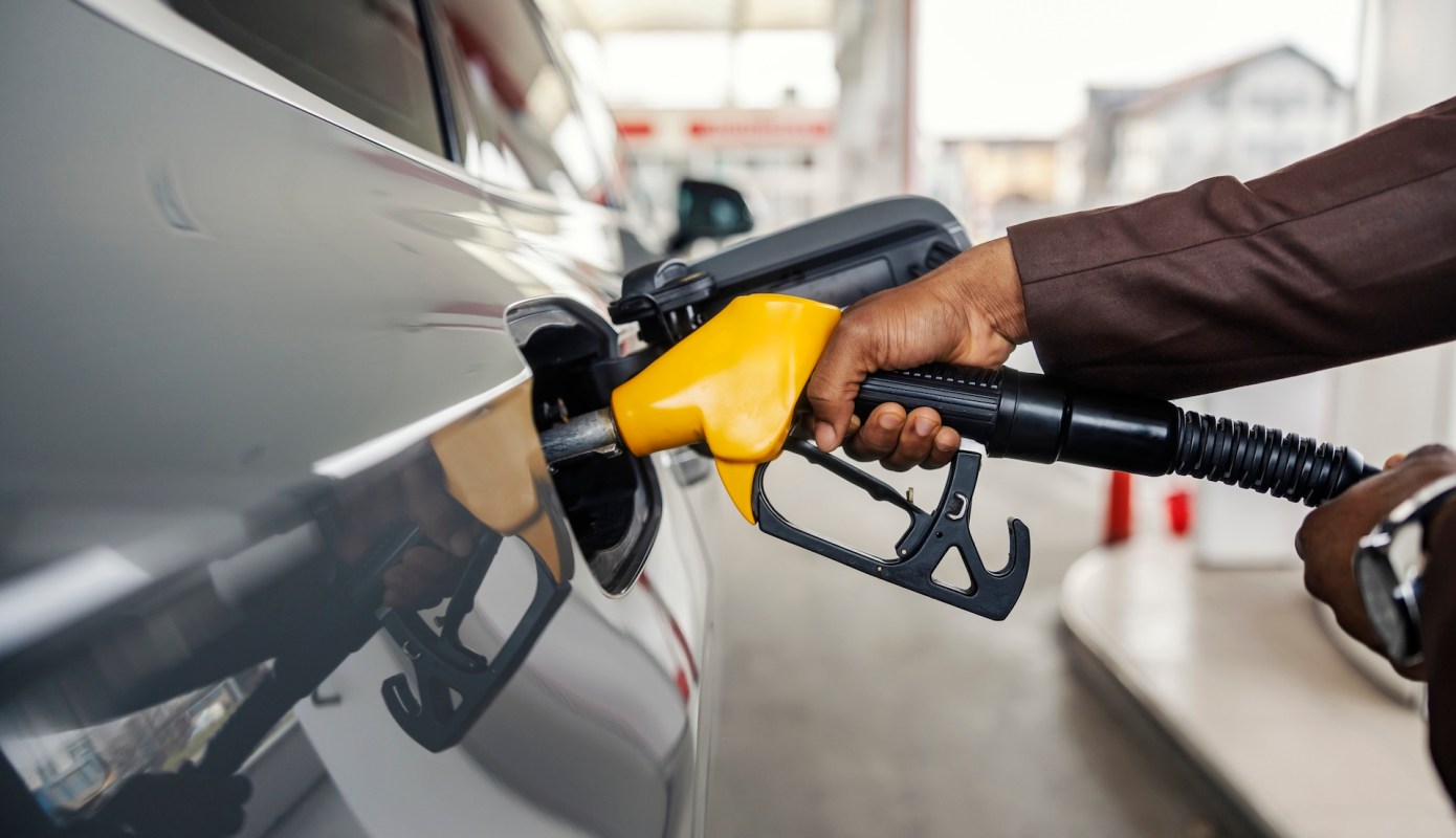 A person refuels a vehicle at a gas station using a yellow fuel nozzle.