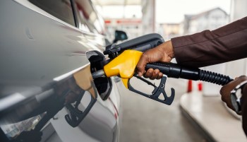 A person refuels a vehicle at a gas station using a yellow fuel nozzle.