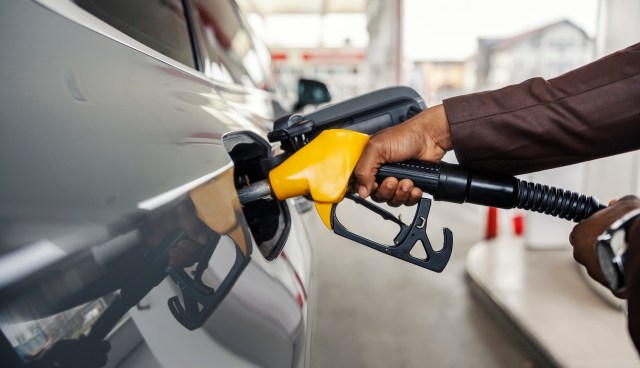 A person refuels a vehicle at a gas station using a yellow fuel nozzle.