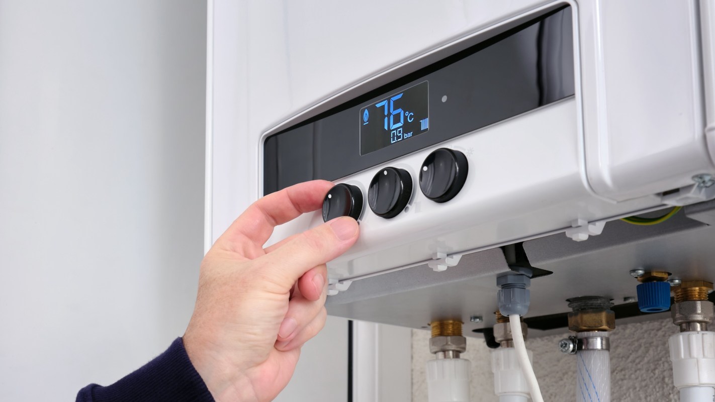 A hand adjusting temperature controls on a boiler.