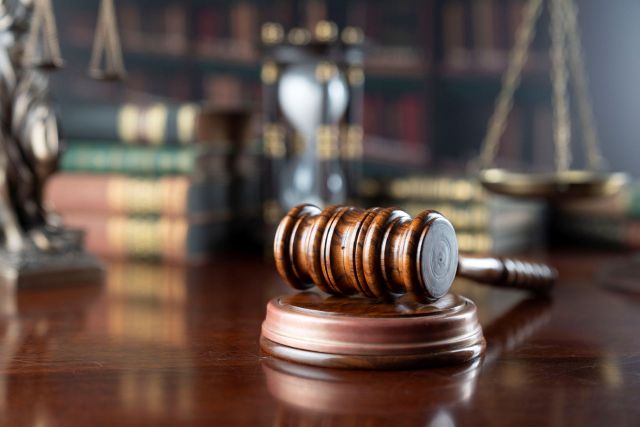 A wooden gavel rests on a polished table with law books and a scale in the background.