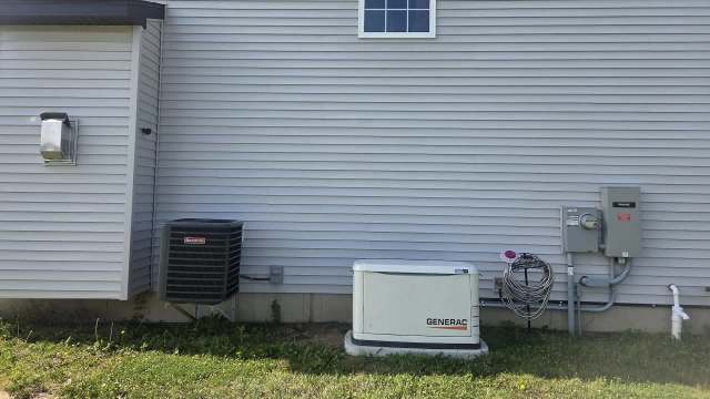 A side view of a house featuring an air conditioning unit and a generator next to utility connections on the wall.