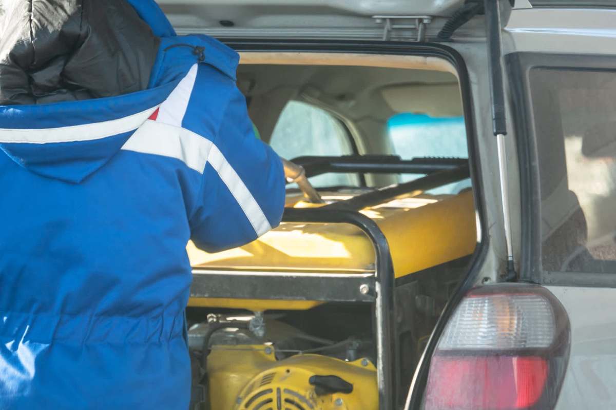 A person in a blue jacket loads a yellow piece of equipment into the back of an SUV.