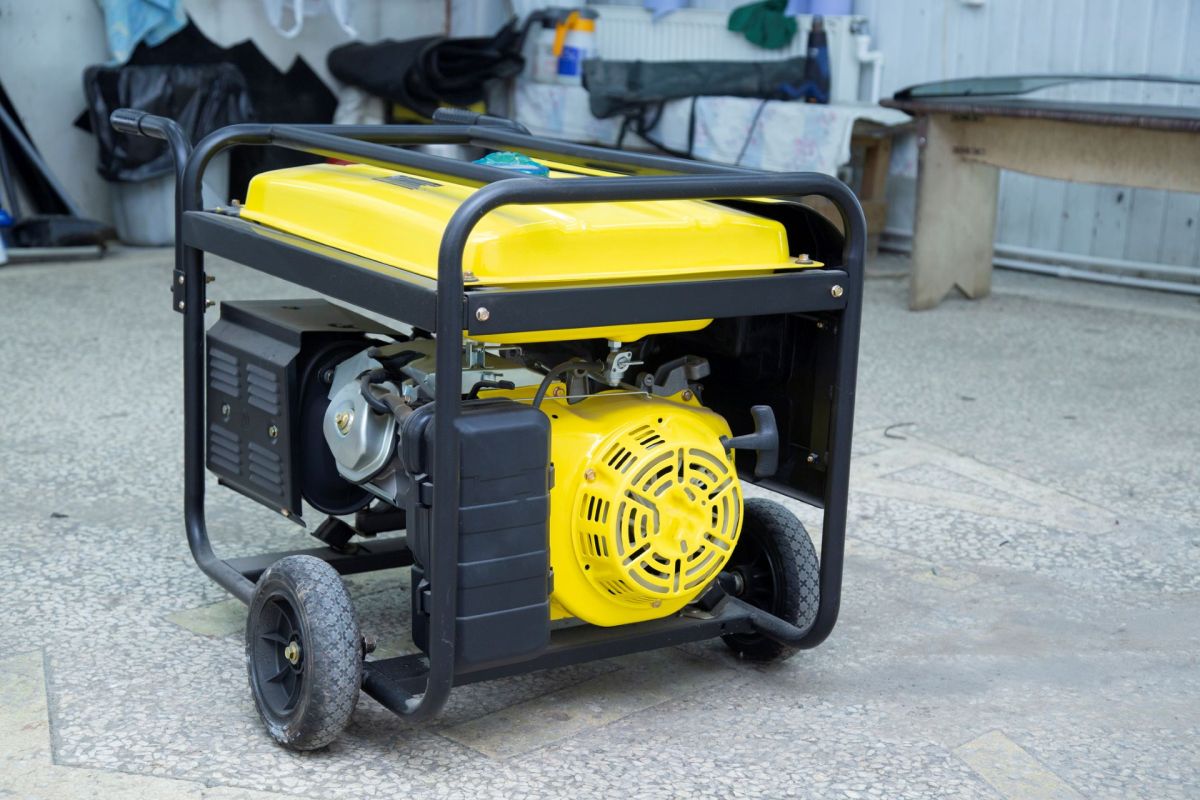 A portable generator with a yellow top and black frame, sitting on a concrete surface.