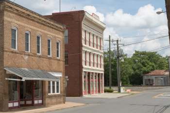 A view of brick buildings at a street corner, with trees and power lines in the background.
