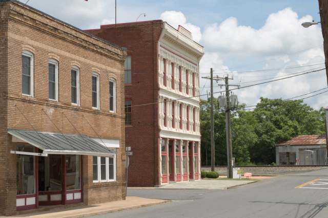 A view of brick buildings at a street corner, with trees and power lines in the background.