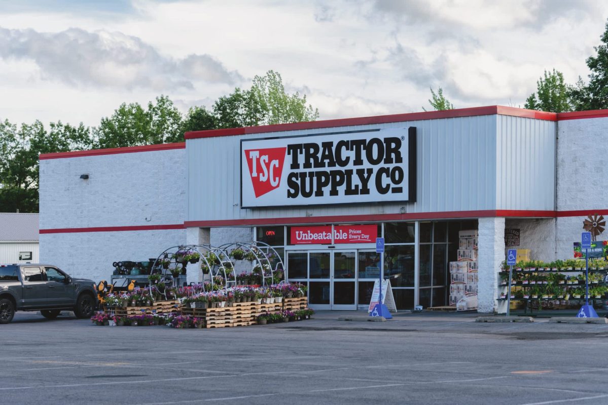 A Tractor Supply Co. store with flower displays outside and a gray pickup truck parked nearby.