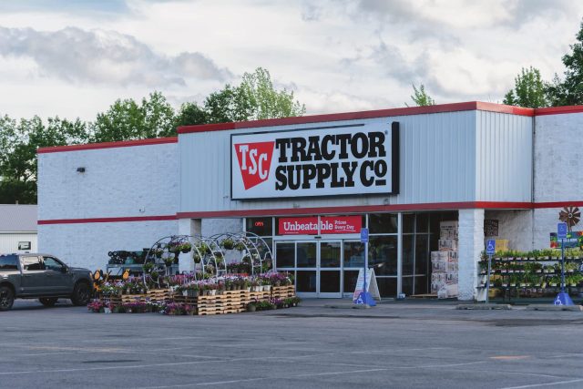 A Tractor Supply Co. store with flower displays outside and a gray pickup truck parked nearby.