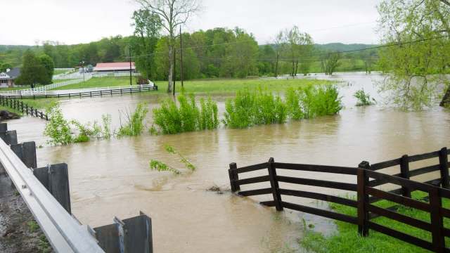 Flooded farmland with submerged trees and a broken wooden fence in a rural area.
