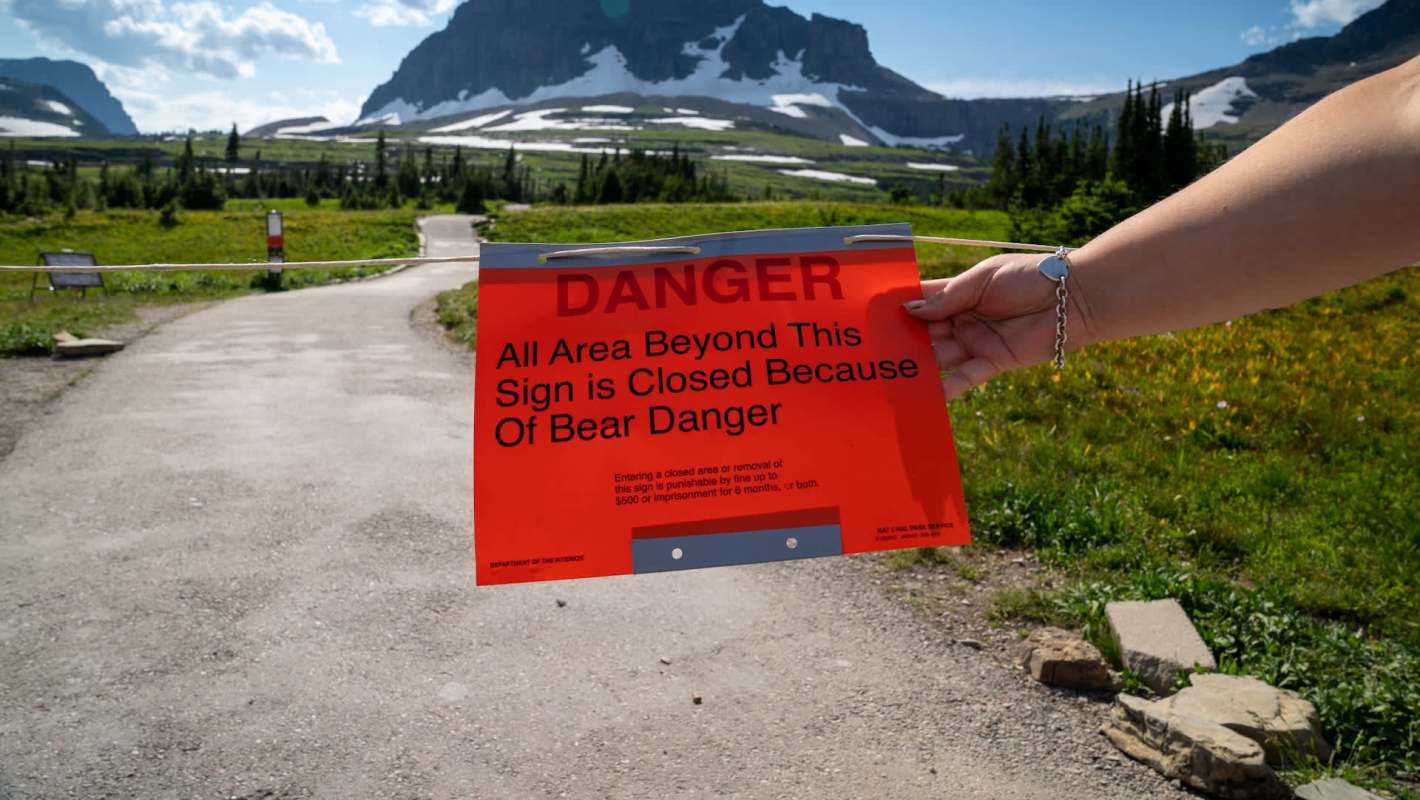 A person holds a bright orange warning sign stating the area is closed due to bear danger.