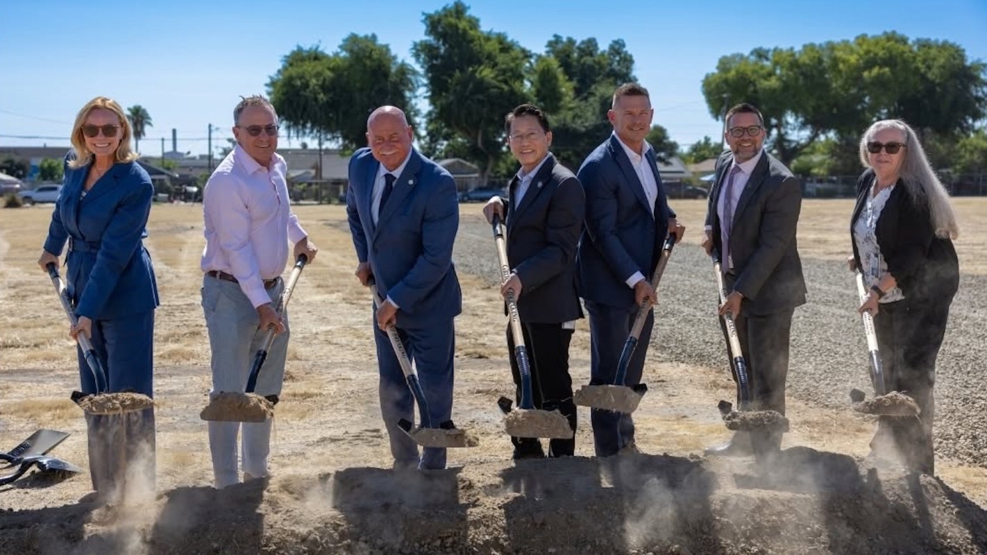 A group of people holds shovels and breaks ground at a construction site.